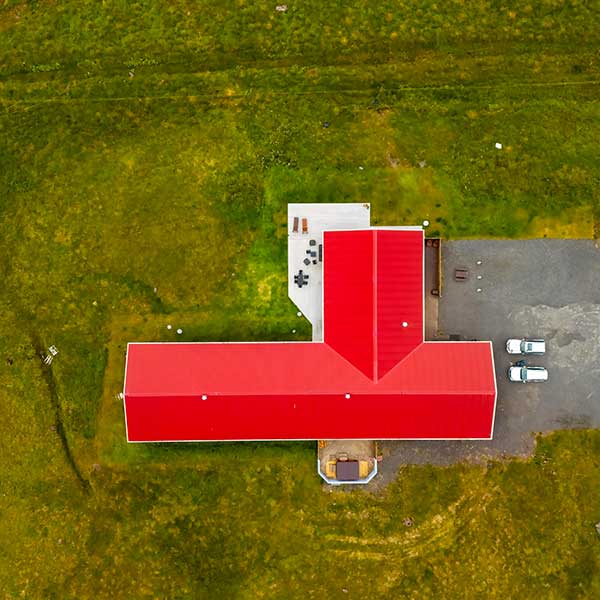 Aerial view of Long Valley Lodge Iceland with a bright red L-shaped roof, surrounded by green grass. Two parked cars and outdoor seating are visible—an inviting spot for Wildside Adventures or fly fishing Iceland enthusiasts. | Belize River Lodge Guided Fishing Trips | Wildside Adventures Travel